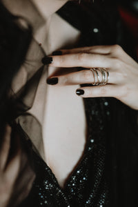 Woman wearing dainty silver stackable rings on her hand with black nail polish and a black dress